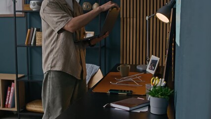 Wall Mural - Medium shot of young Asian male freelancer sitting down at table while starting working day with laptop in cozy home office