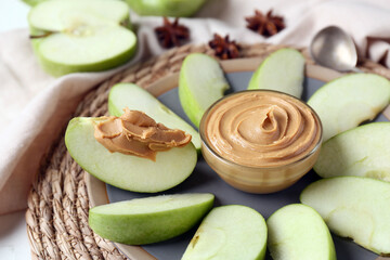 Wall Mural - Plate with fresh apple slices and bowl of sweet peanut butter on white background, closeup