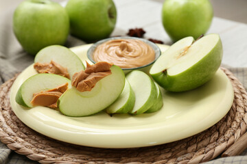 Wall Mural - Plate with cut fresh apple and bowl of sweet peanut butter on white wooden background, closeup