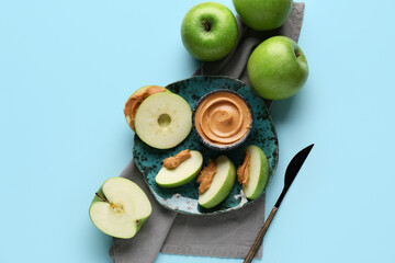 Wall Mural - Plate of fresh apple slices with sweet peanut butter on blue background