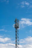 ogromny stalowy maszt telekomunikacyjny z licznymi nadajnikami i antenami zamontowanymi na szczycie. w tle błękitne niebo z nielicznymi chmurami