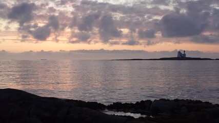 Wall Mural - sunset over Averoya sea with pink sky, calm waters, and distant lighthouse on a small rocky island