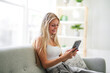 © Louis-Paul Photo - Portrait beautiful smiling young woman at home on sofa using cellphone