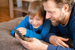 © Marina Demidiuk - Father and son little boy laughing and using phone. They watching funny videos together, playing games on smartphone. Concept technology, smart phone addicted. Fun weekend activity. Modern fatherhood