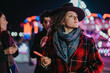 © qunica.com - Friends gathered during a vibrant winter night, enjoying sweets and the festive atmosphere of a lively outdoor carnival with vibrant lights and colorful backgrounds.