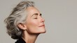 © Tina - A senior Caucasian woman with gray hair smiles gently, eyes closed, showcasing a serene expression against a neutral background.