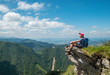© Soloviova Liudmyla - Dressed trekking clothes hiker woman sitting on rocky cliff enjoying green valley at Mala Fatra mountain range, Slovakia. Active people and European tourism concept image.