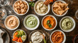 © Aditya - A colorful assortment of dips and snacks, including various hummus flavors, vegetable sticks, and crackers, artfully arranged on a wooden surface.