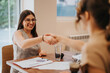 © qunica.com - Bright and positive meeting between two businesswomen, with smiling faces and handshake, showing successful collaboration and professional networking in a comfortable office environment.