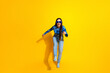 © deagreez - Cheerful woman posing playfully in modern fashion against vibrant yellow background, expressing energy and positivity
