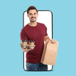 © New Africa - Food delivery service worker giving online order out of mobile phone display. Light blue background