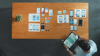 Top down view of software developer holding tablet while choosing icon for mobile phone interface or software program. Start up manager using Ux Ui design to develop wireframe prototype. Convocation.