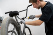 © Mihail - A person is carefully installing new bicycle handlebars in a workshop, using a screwdriver while wearing gloves. The bike rests on a stand for easy access.