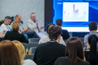 © Anton Gvozdikov - Audience attentively watching professional presentation in conference setting with speaker and screen.