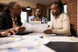 © DC Studio - African american entrepreneurs with documents discussing and consulting around meeting table in brick wall office. Startup team planning business project together and working towards an agreement.