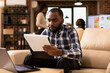 © DC Studio - Male analyst checks printed notes and monitors company research data on laptop during marketing strategy planning. Businessman studies corporate documents on clipboard, reviewing financial charts.