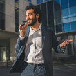 © Miljan Živković - Smiling businessman sending a vocal message on his phone in front of modern office buildings