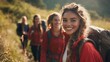 © Arslan - A group of young women hiking through a grassy field with backpacks and bright red jackets smiling at the camera