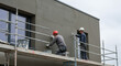© Item.io - Two construction workers apply stucco to a modern building's exterior wall using scaffolding.
