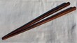 © Watcharaporn - Traditional Wooden Chopsticks Flat Angle Close Up Texture Design Dark Brown and Red Finish On Light Fabric Surface