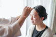 © Masakazu Tokashiki - A woman is getting her hair done by a stylist. The stylist is putting makeup on the woman's face