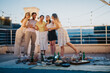 © qunica.com - A group capturing memories on a rooftop decorated with lights, enjoying vibrant company and a picnic.