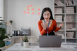 © Tj - Excited businesswoman wearing an orange shirt and id card is celebrating success during a video call in the office, gesturing with her hands and showing enthusiasm