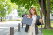 © maeching - Asian businesswoman in suit smiling holding smartphone and documents as she walks through modern business building