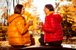 Two young women enjoying a conversation outdoors during an autumn day in the park while sipping hot coffee