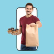 © New Africa - Food delivery service worker giving online order out of mobile phone display. Light blue background
