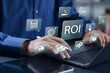 © Pakin - ROI, Return on Investment concept. financial strategies, marketing plan, and efficiency. business strategy for investment. Businessman using laptop with ROI icons on virtual screen.