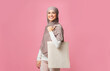 © Prostock-studio - Eco shopping. Cheerful arabic girl in hijab posing with tote canvas shopper bag with place for mockup, pink background