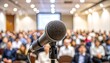 © Gema - A microphone in focus, positioned in front of a large audience in a conference hall