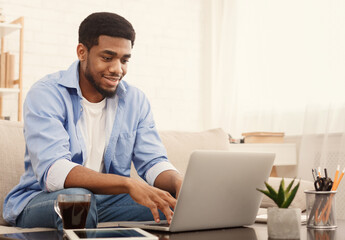 Millennial african-american man working on laptop in home office, typing plan of new startup project, copy space