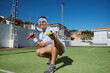 © Taras Grebinets - Smiling Female Tennis Player Holding a Ball on a Sunny Day