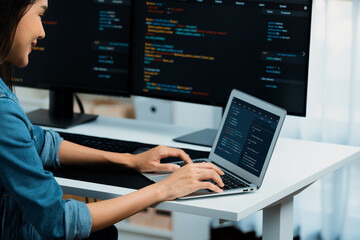 Smiling young Asian in IT developer creating with typing online information on laptop with coding program data of application, wearing jeans shirt. surrounded by safety analysis two screen. Stratagem.