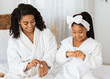 © Prostock-studio - Cute Little African Girl And Her Young Mom Doing Hand Beauty Treatment At Home, Applying Moisturising Body Cream While Sitting On Bed In Bathrobes, Mother And Daughter Having Domestic Spa Day, Closeup