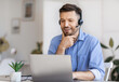 © Prostock-studio - Business Education. Handsome young businessman in headset watching webinar on laptop in modern office, having online training, looking at computer screen with interest, sitting at desk, copy space