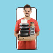 © New Africa - Food delivery service worker giving online order out of mobile phone display. Light blue background