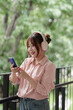 © snowing12 - Asian adult woman happy listening music wearing headphones using mobile phone outdoors park green environment freelance lifestyle casual relax
