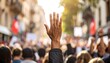 © Fera - A hand raised in a crowd during a protest. Sunlight streams through the blurred background