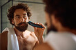 © Drazen - Mature man using electric razor while shaving in bathroom.