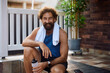 © Drazen - Happy athletic man with water bottle relaxing on porch steps during home workout and looking at camera.