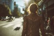 Woman wearing fringe leather jacket walking sunlit city street full frame buildings visible wide shot