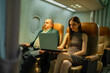 © Wanwajee - Smiling overweight businessman seated next to woman working on computer during flight. Idea of inflight productivity, business trip, technology use, airline service, and international travel industry.
