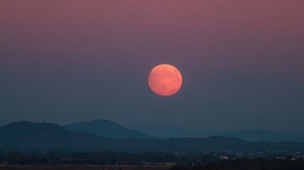 Wall Mural - A full moon rises majestically above distant mountains during twilight, casting a warm glow over the tranquil landscape and enhancing the beauty of the evening sky.