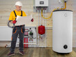© Grispb - Heating installation, plumber engineer checking blueprints near boiler system, hot water tank, central heating, household utilities maintenance