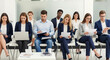 © KAMAPAN - Group of male and female job seekers sitting in row on chairs waiting for job interview. Young people holding paper documents and resumes, using laptop, waiting their turn. Human resources, employment