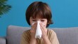 © pkproject - Young boy with cold or flu symptoms resting on couch at home and blowing his nose with a tissue