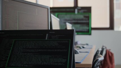 Screens of desktop computers with coded information or programming language standing on desks in classroom of modern school for kids studying information technology